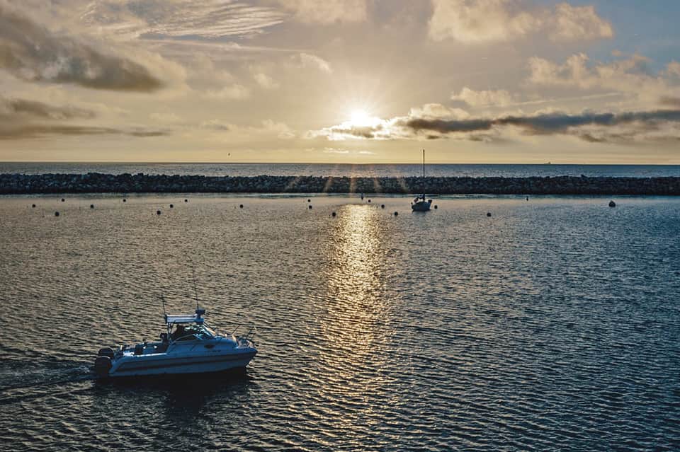 Serene harbor sunset with sailboats anchored in calm blue water and dramatic sky