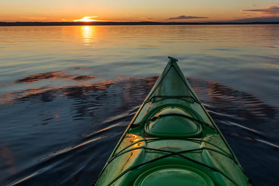 Green kayak on calm water at sunset with golden light reflecting on surface