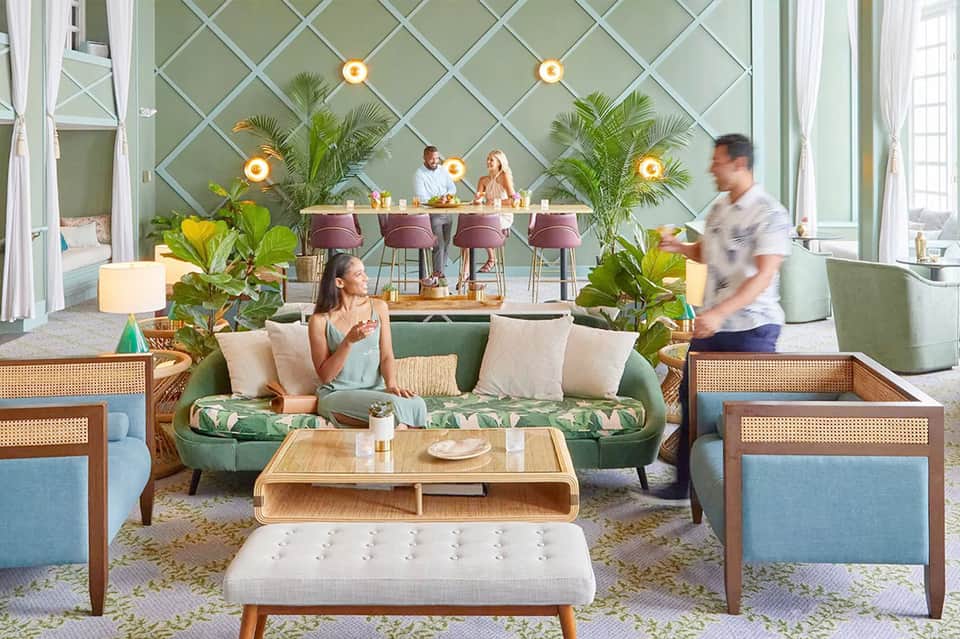 Modern resort lounge with green curved sofa, potted plants, dining area, and floor-to-ceiling windows