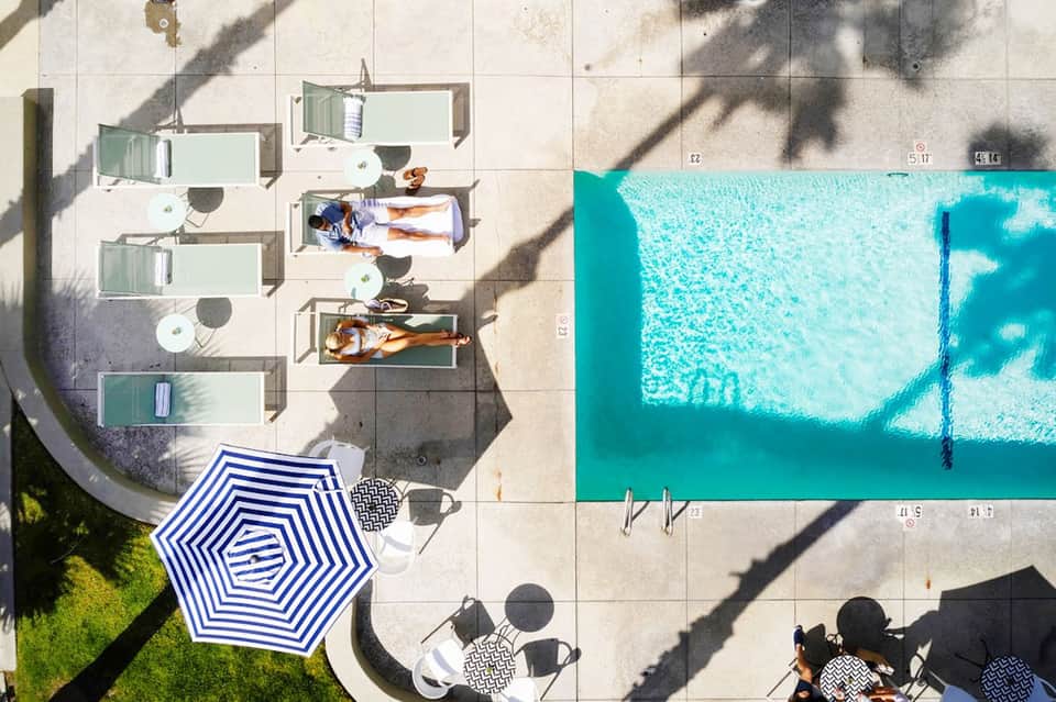 Aerial view of resort pool deck with sunbathing guests, lounge chairs, umbrellas, and turquoise pool