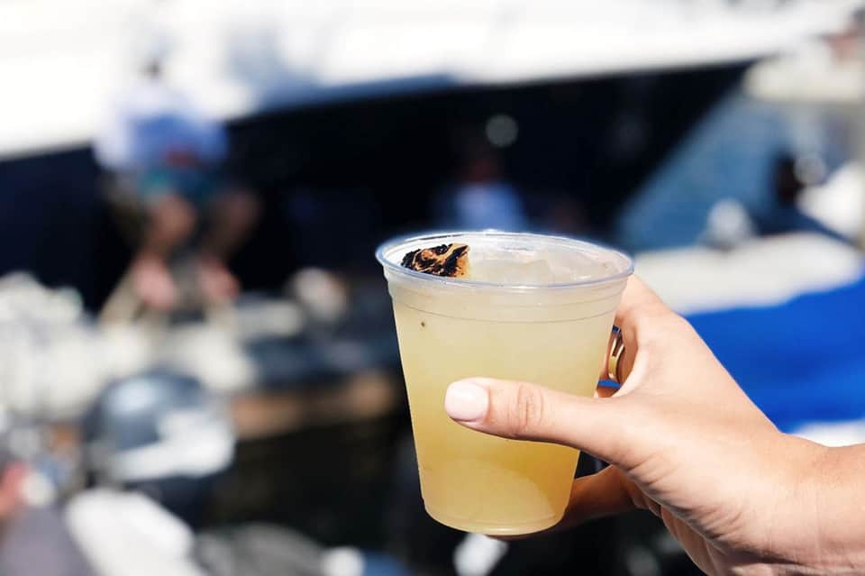 Hand holding a clear cup with pale yellow beverage and ice at a beach resort venue