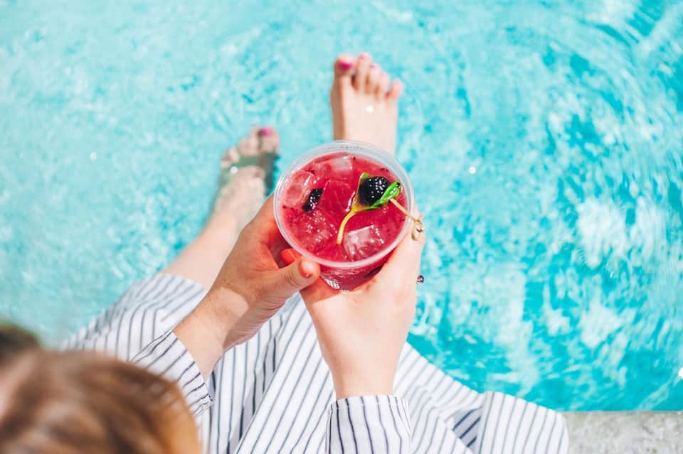 Person holding colorful cocktail with berries while relaxing in pool