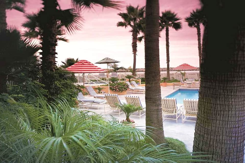 Beachfront pool area with loungers, palm trees, and ocean view at sunset