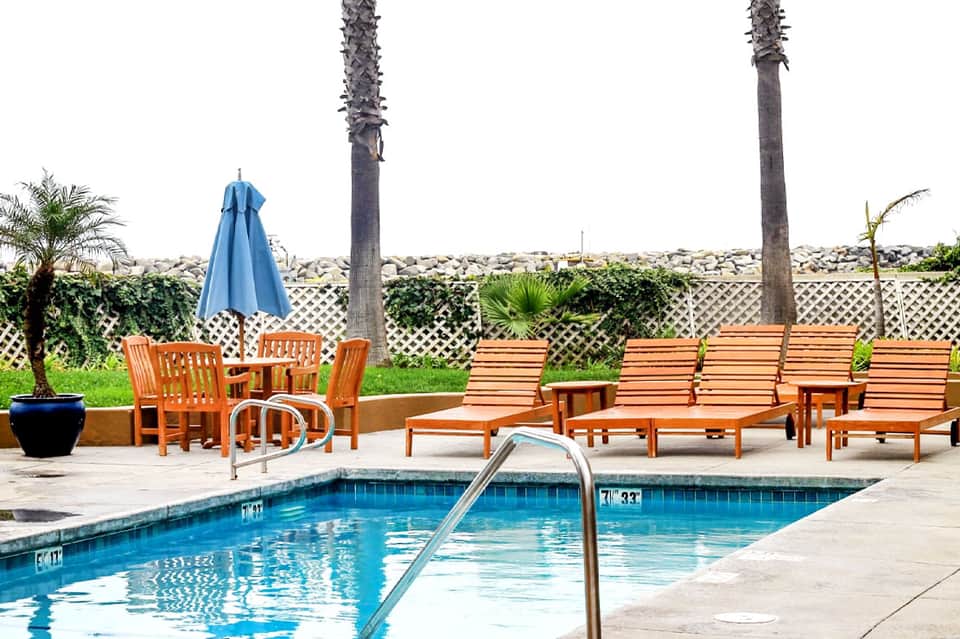 Resort spa pool with wooden lounge chairs, blue umbrella, and decorative rock wall backdrop