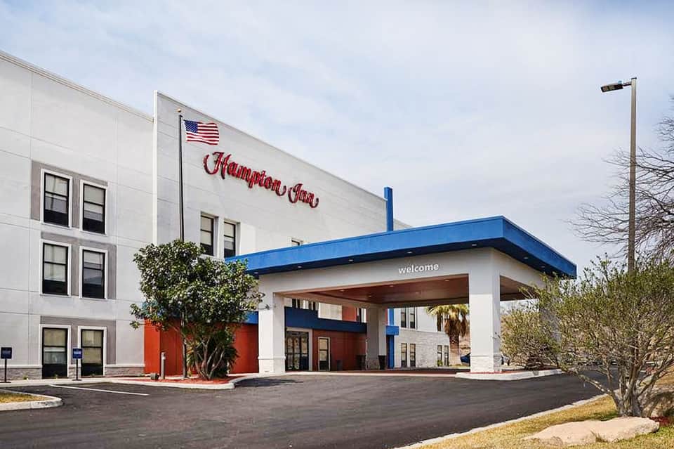 Hampton Inn hotel exterior with white and blue awning, American flag, and welcoming entrance