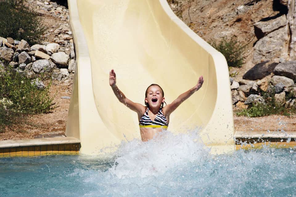 Child splashing down a white water slide into a turquoise pool at a resort