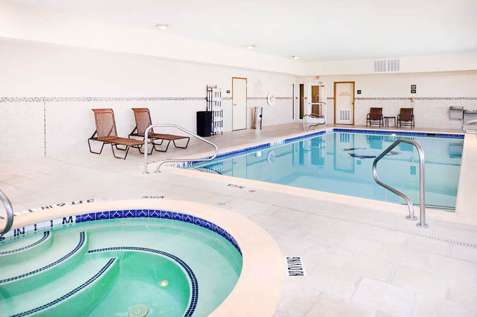 Indoor pool facility with spa tub and lounge chairs in bright, clean recreation area