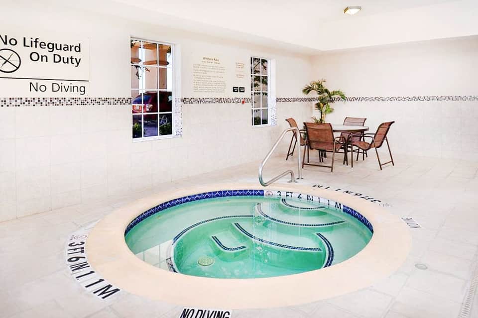 Indoor circular hot tub with turquoise water in bright room with tile walls and safety signage