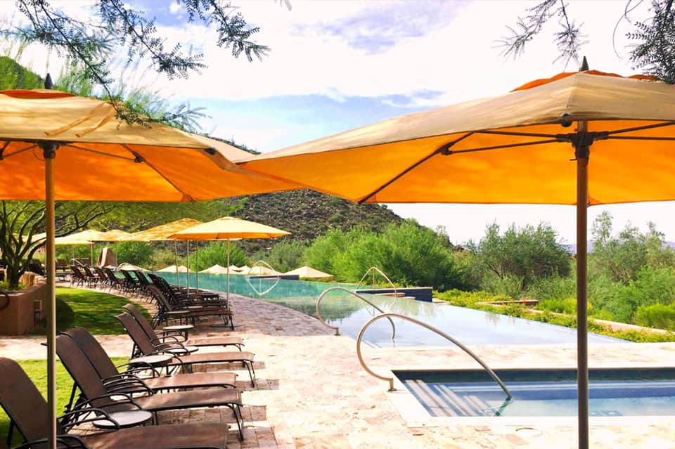 Resort pool area with orange cantilever umbrellas and lounge chairs overlooking hills and water features