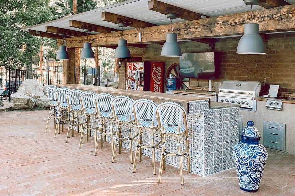 Outdoor bar and grill area with blue and white bistro chairs beneath wooden pergola structure