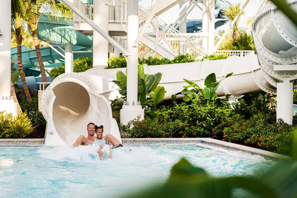 Adult and child enjoying water slide exit at resort pool with white architectural elements