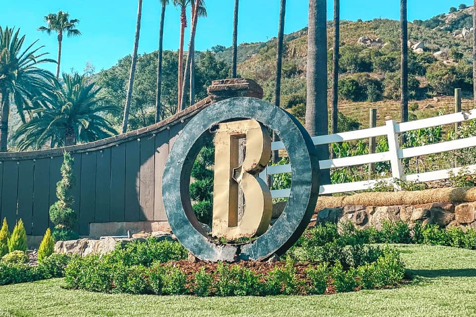 Large decorative 'B' monument at entrance gate with palm trees and landscaped grounds