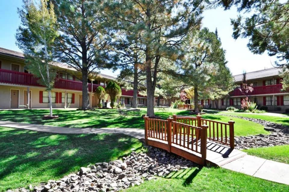 Motel courtyard with wooden bridge, red-roofed buildings, and mature trees