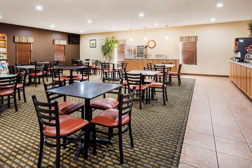 Hotel breakfast room with black chairs, coral cushions, and wooden counter service area