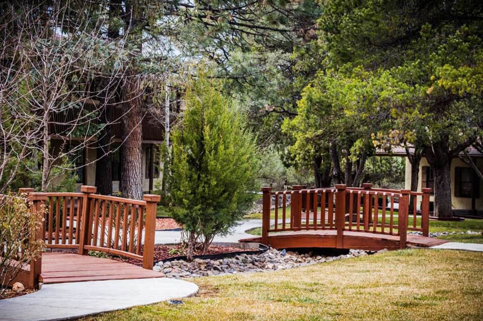 Wooden pedestrian bridge over landscaped grounds with mature trees and residential buildings