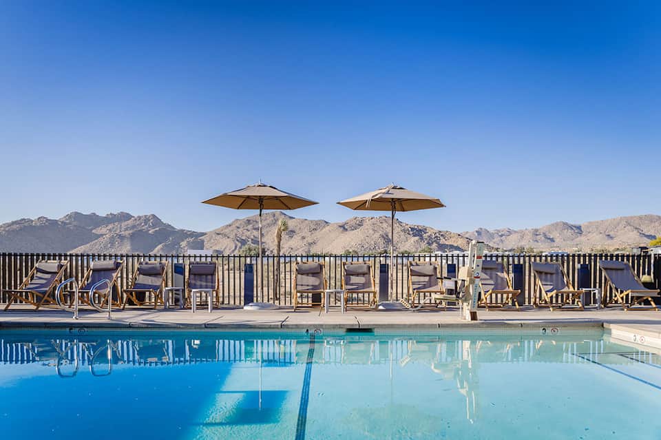 Resort pool with lounge chairs and umbrellas overlooking desert mountains under clear blue sky