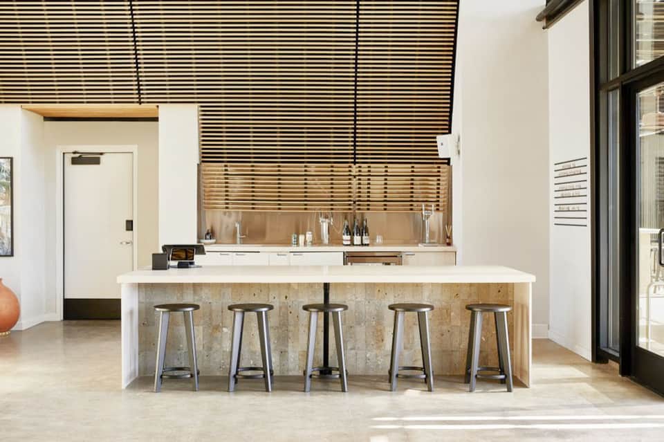 Contemporary kitchen with white island, bar seating, wooden slat backsplash, and stainless steel appliances