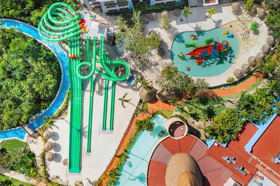 Aerial view of a colorful water park with green slides, lazy river, and multiple pools