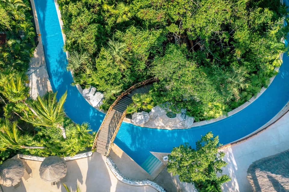 Overhead view of curved lazy river with lush green jungle vegetation and wooden boardwalk pathway