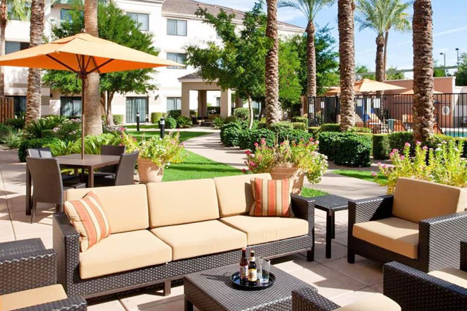 Resort courtyard with comfortable seating, orange umbrellas, palm trees, and lush landscaping