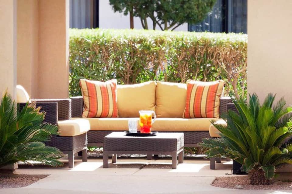 Patio seating area with wicker furniture, yellow cushions, and hedge backdrop