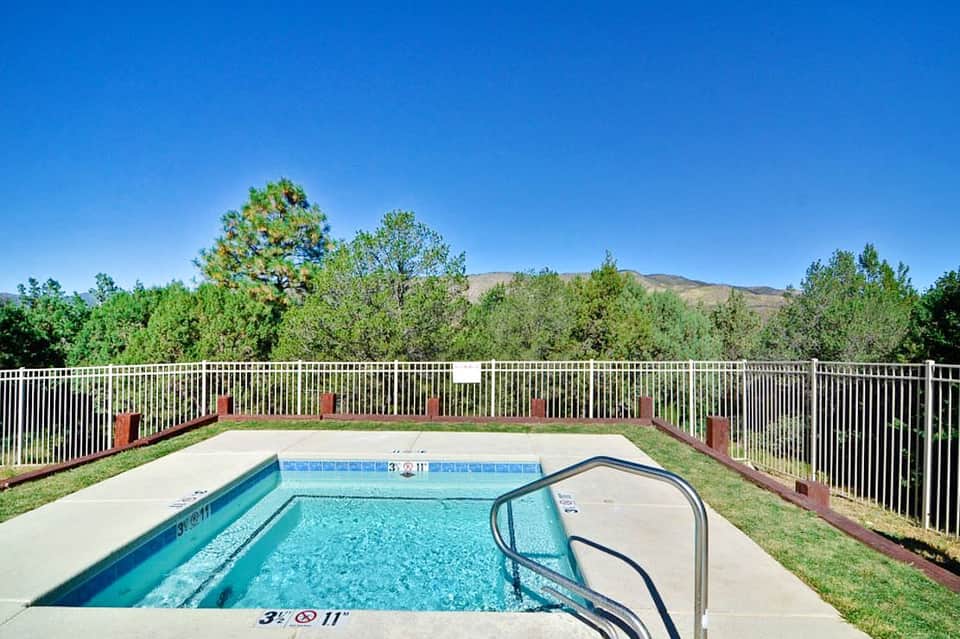 Outdoor swimming pool with white safety railing surrounded by green trees and mountains