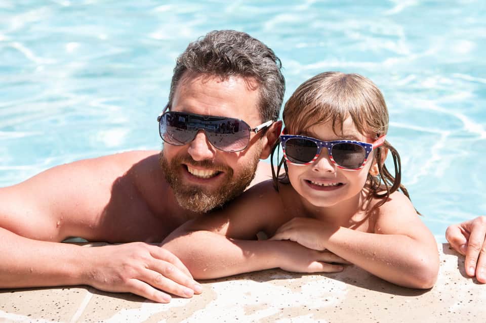 Father and child in pool wearing sunglasses and smiling at camera