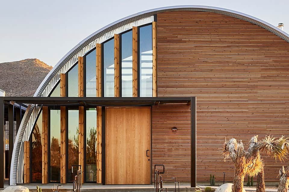 Modern curved wood and metal building with large windows and desert landscaping