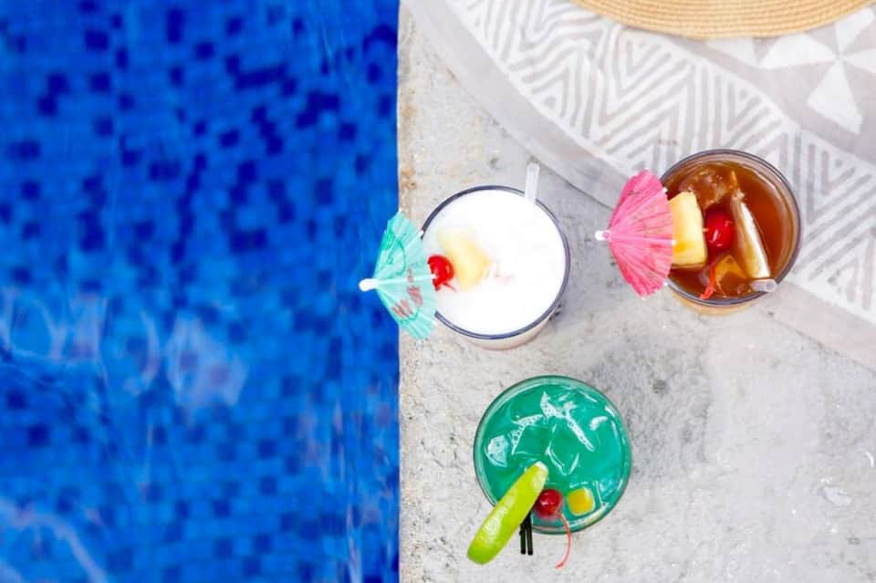 Overhead view of three colorful tropical cocktails by a bright blue pool
