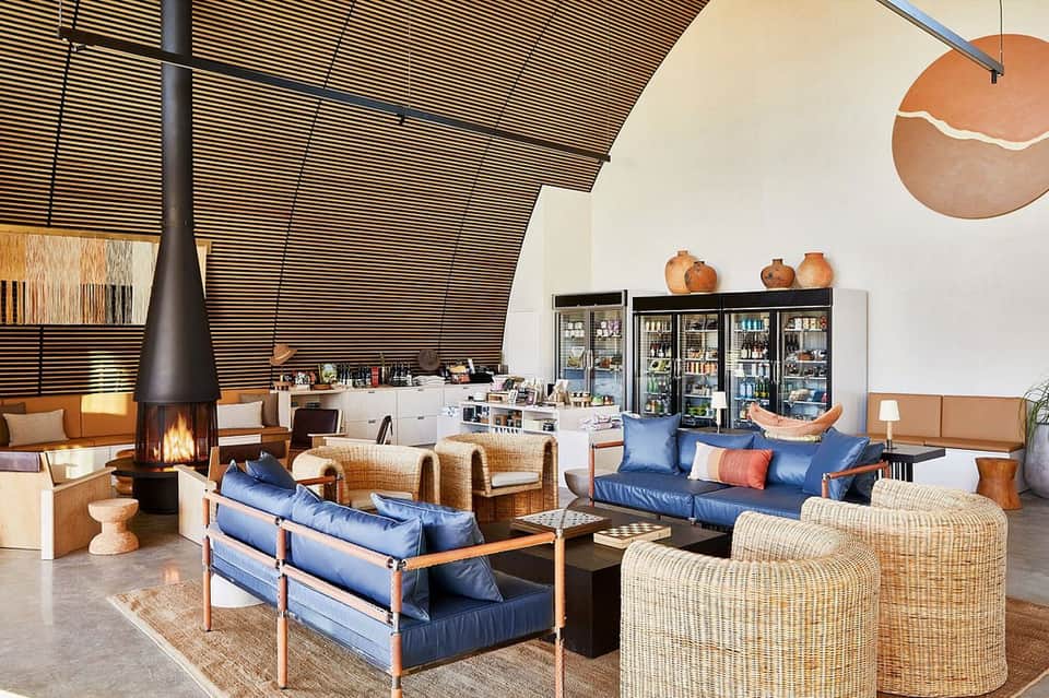 Modern resort lobby with fireplace, blue seating, woven chairs, and minimalist decor
