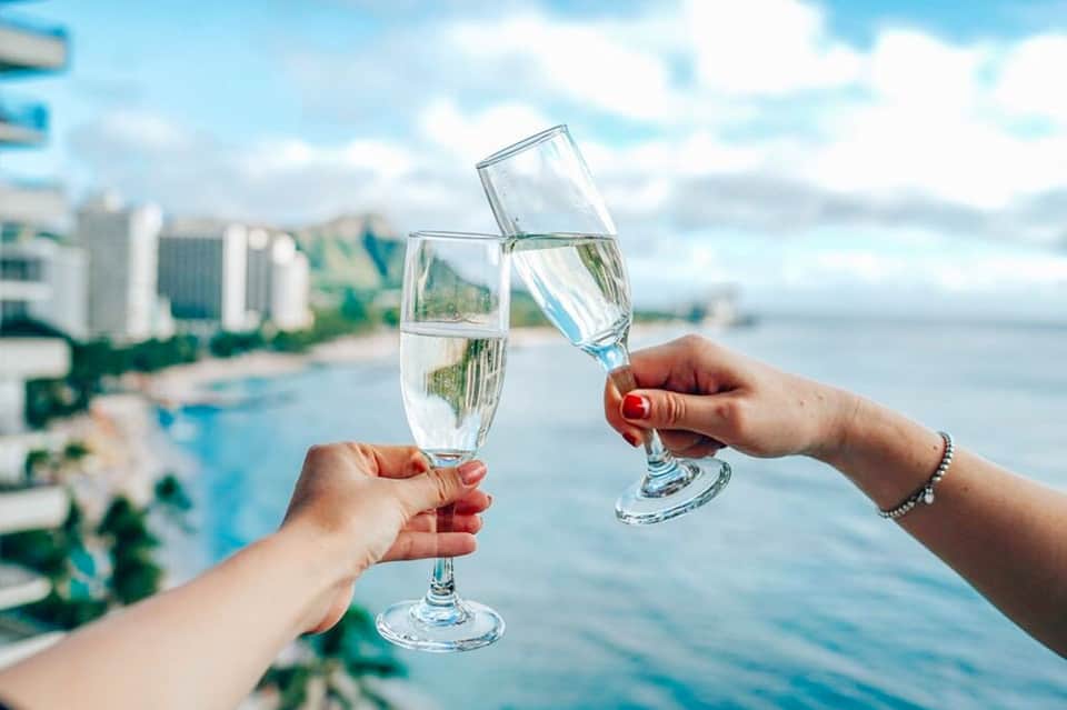 Two people toasting with water glasses overlooking a coastal beach town with high-rise hotels
