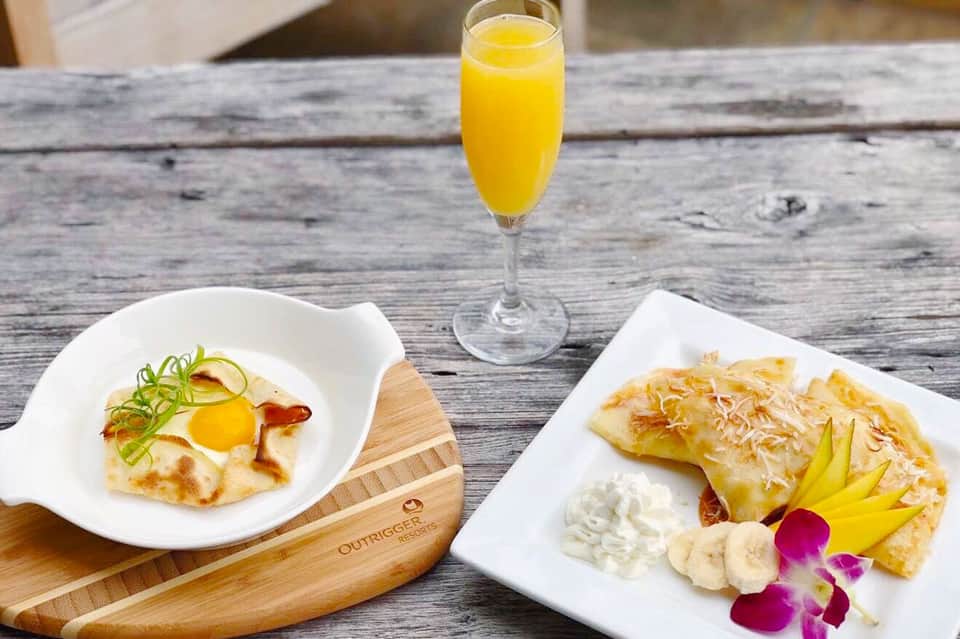 Gourmet breakfast plate with egg dish, pastry, and fresh fruit served with orange juice on wooden table