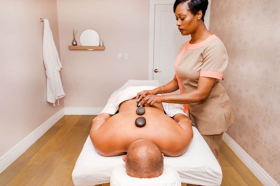 Spa massage therapist performing hot stone treatment on client in calm, neutral-toned room