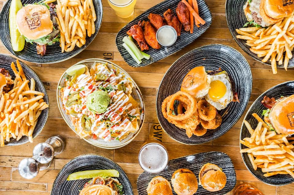 Overhead view of restaurant table with burgers, onion rings, wings, and appetizers