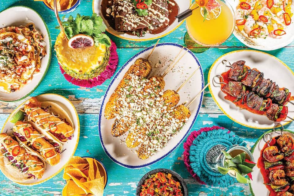 Vibrant overhead view of colorful Mexican dishes and fresh juices on turquoise table