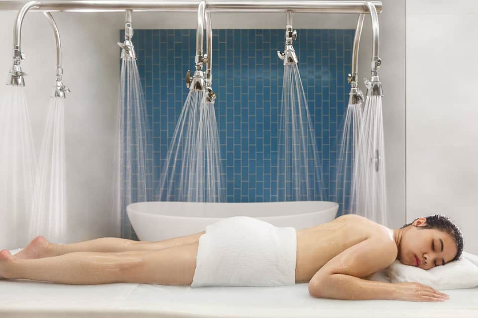 Spa treatment area with rainfall showerheads and tiled accent wall behind a white soaking tub