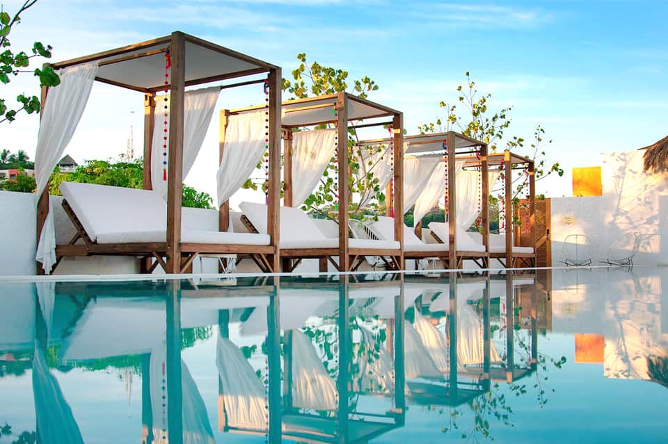 Luxury resort pool cabanas with white curtains reflected in turquoise water at sunset