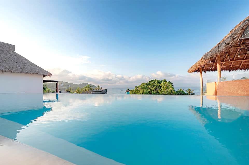 Infinity pool with thatched-roof bungalows overlooking tropical ocean and islands