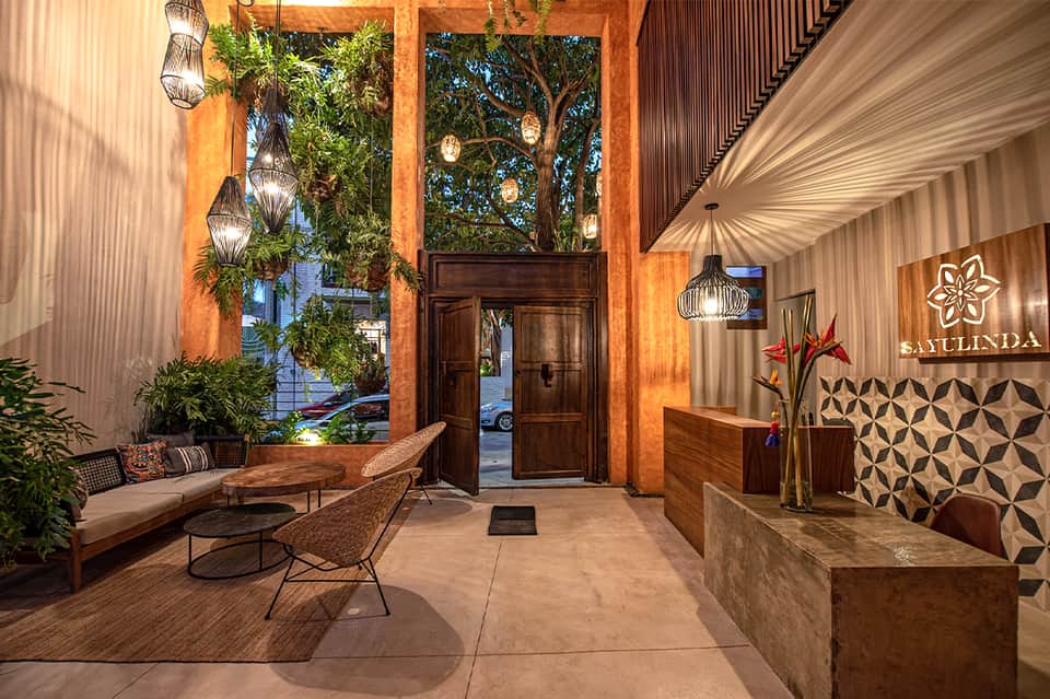 Contemporary hotel entrance with wooden doors, hanging lanterns, and tropical plants