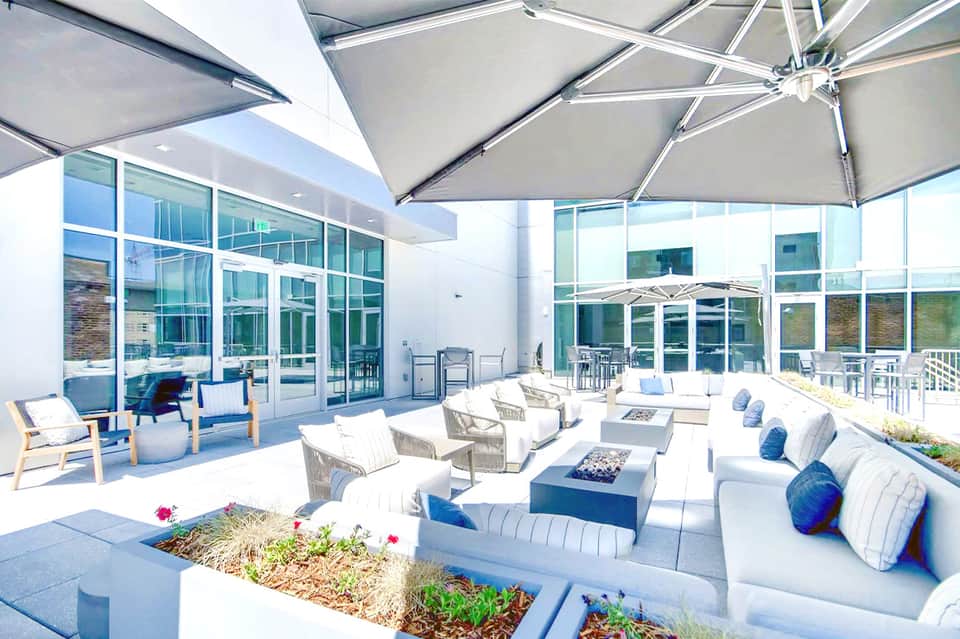 Modern outdoor terrace with white umbrellas, lounge seating, and floor-to-ceiling windows
