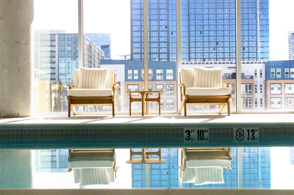 Modern lounge chairs by indoor pool overlooking city skyline and tall buildings