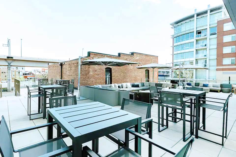 Modern rooftop terrace with dining tables, umbrellas, and city views surrounded by brick buildings