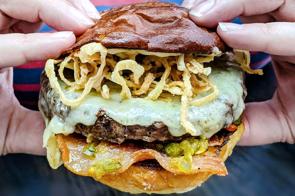 Gourmet burger with crispy onion strings and melted cheese held in hands