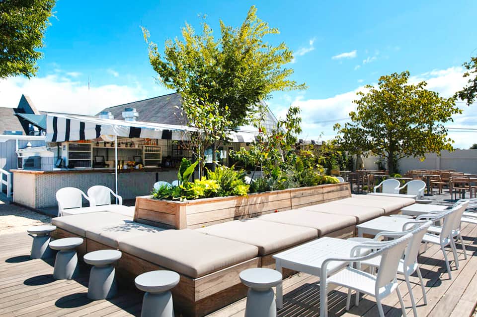 Resort rooftop deck with casual seating, striped cabana, bar counter, and manicured landscaping