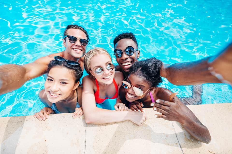 Group of diverse children smiling in bright turquoise swimming pool wearing goggles