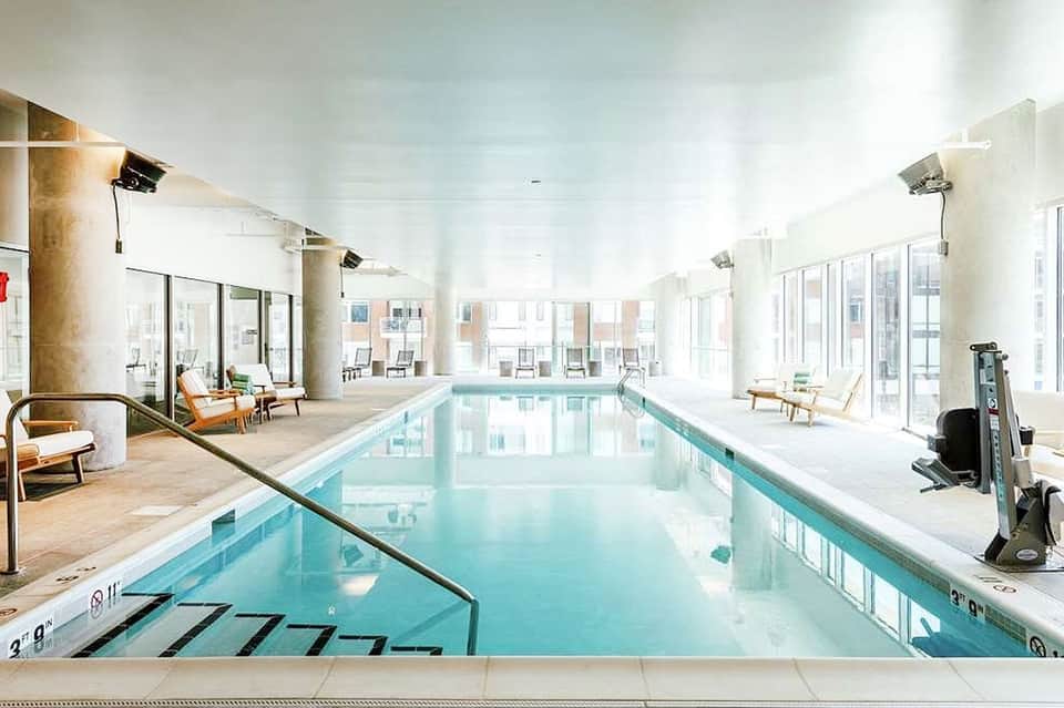 Indoor lap pool with bright natural lighting, lounge chairs, and modern amenities
