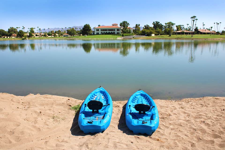 Two blue kayaks on sandy beach with calm lagoon water and resort buildings in background