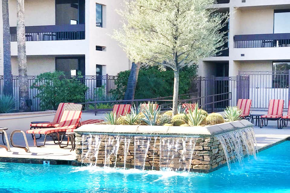 Resort pool with waterfall feature, striped lounge chairs, and multi-story residential buildings