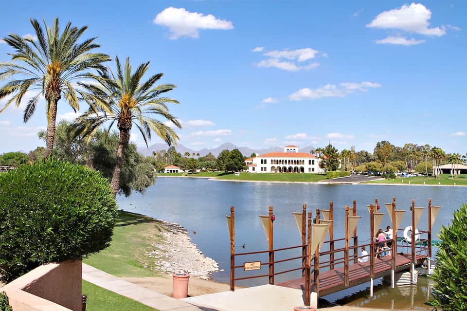 Waterfront resort with white building and red roof across a lake, palm trees, wooden dock
