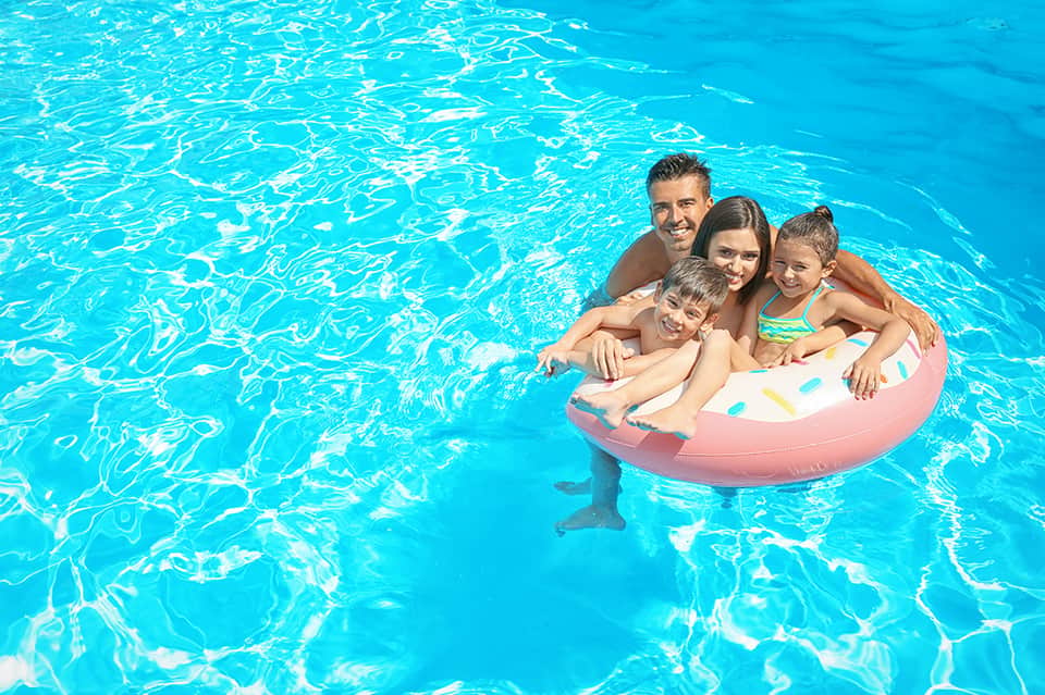 Family of four on pink inflatable raft in bright turquoise swimming pool